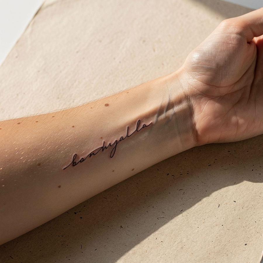 Healed fine-line tattoo on a forearm at fourteen months, photographed in daylight